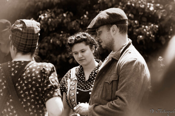 Ein Mann und zwei Frauen in Kleidung aus den 1940er Jahren im Gespräch. Sepiatonung.